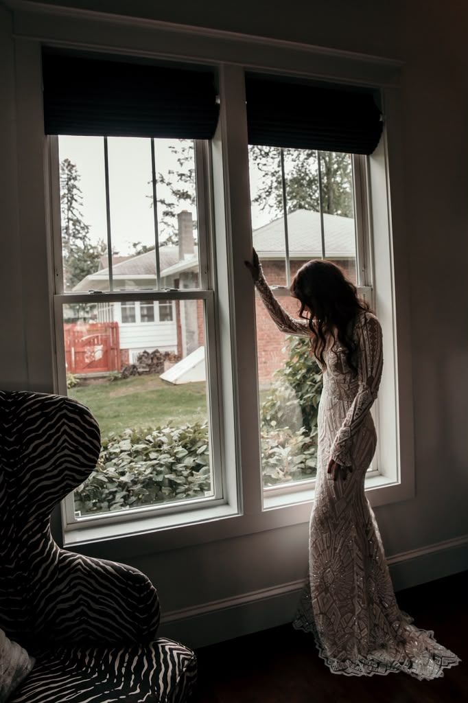 Bride in a beaded gown silhouetted against tall windows