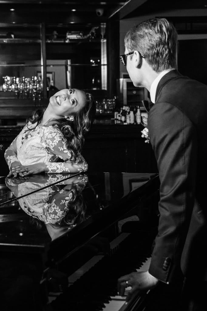 Black and white bride laughing on a grand piano beside the groom
