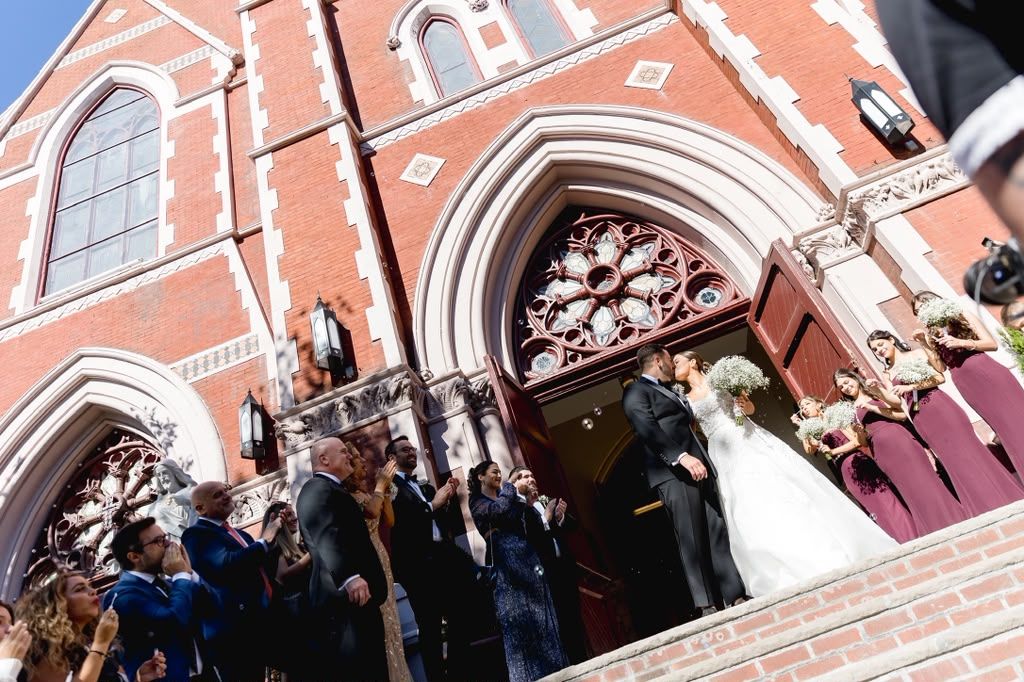 Newlyweds kissing on red brick church steps as guests cheer