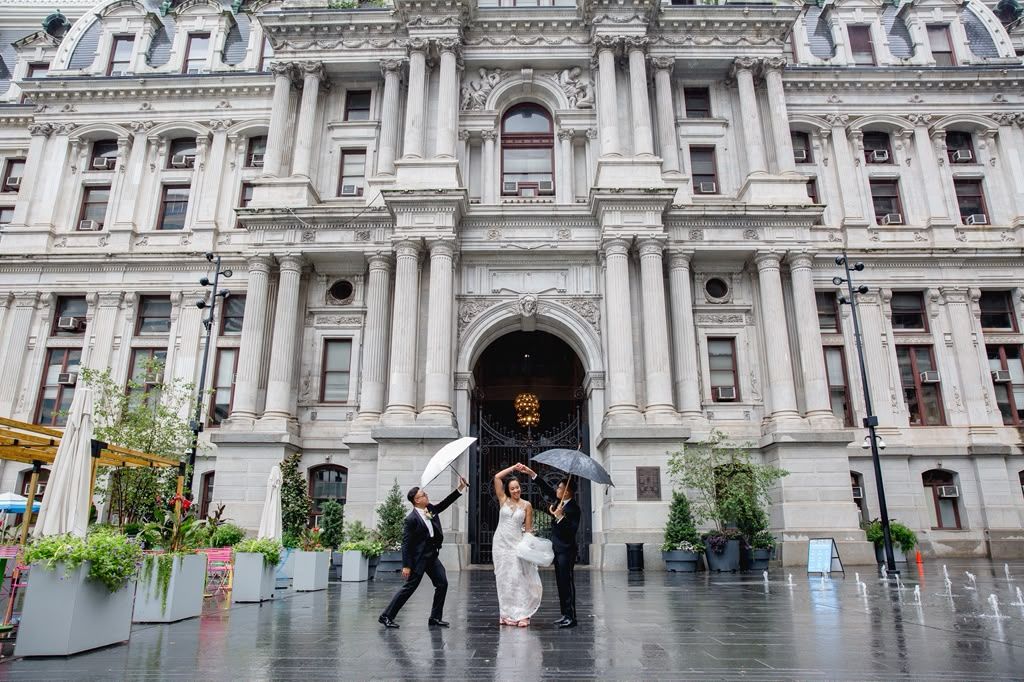 Couple with umbrellas in front of an ornate city hall on a rainy day