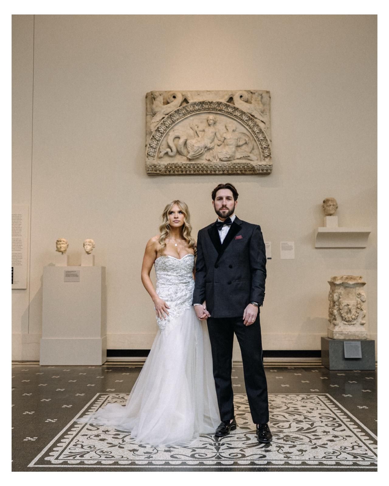 Bride and groom standing in a classical museum hall with marble relief