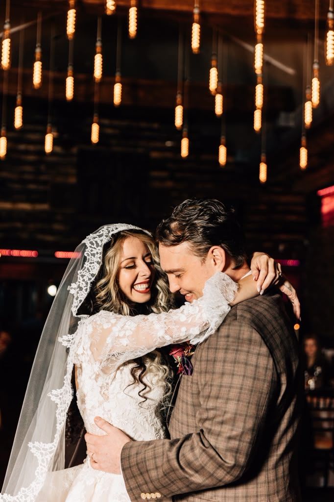 Laughing couple embracing beneath glowing Edison bulbs