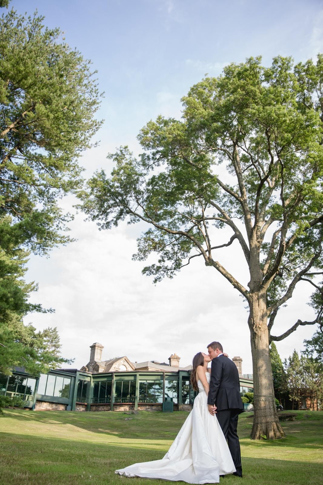 Couple kissing beneath a towering oak on an estate lawn