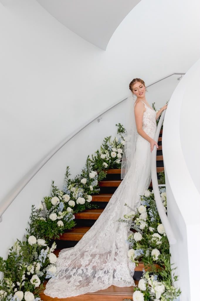 Bride on a spiral staircase lined with white flowers and greenery