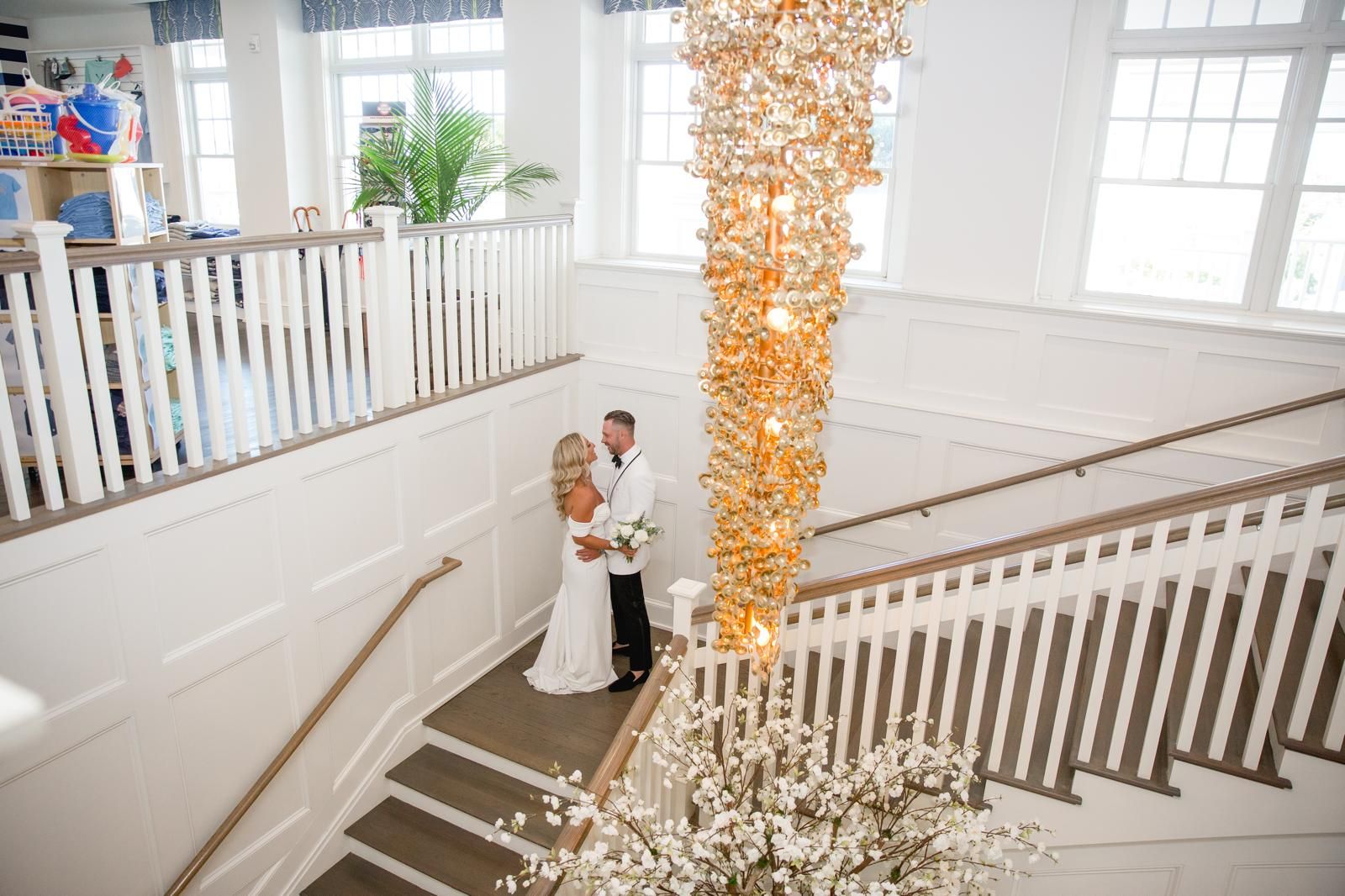 Bride and groom on a white staircase beneath a golden chandelier
