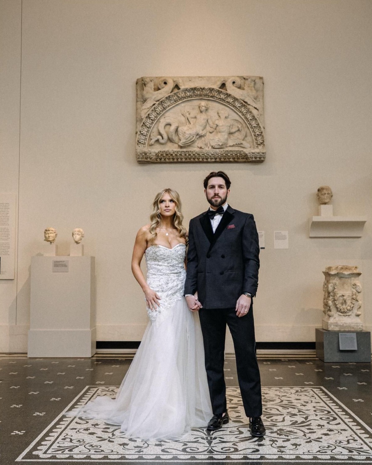 Bride and groom standing in a classical museum hall with marble relief