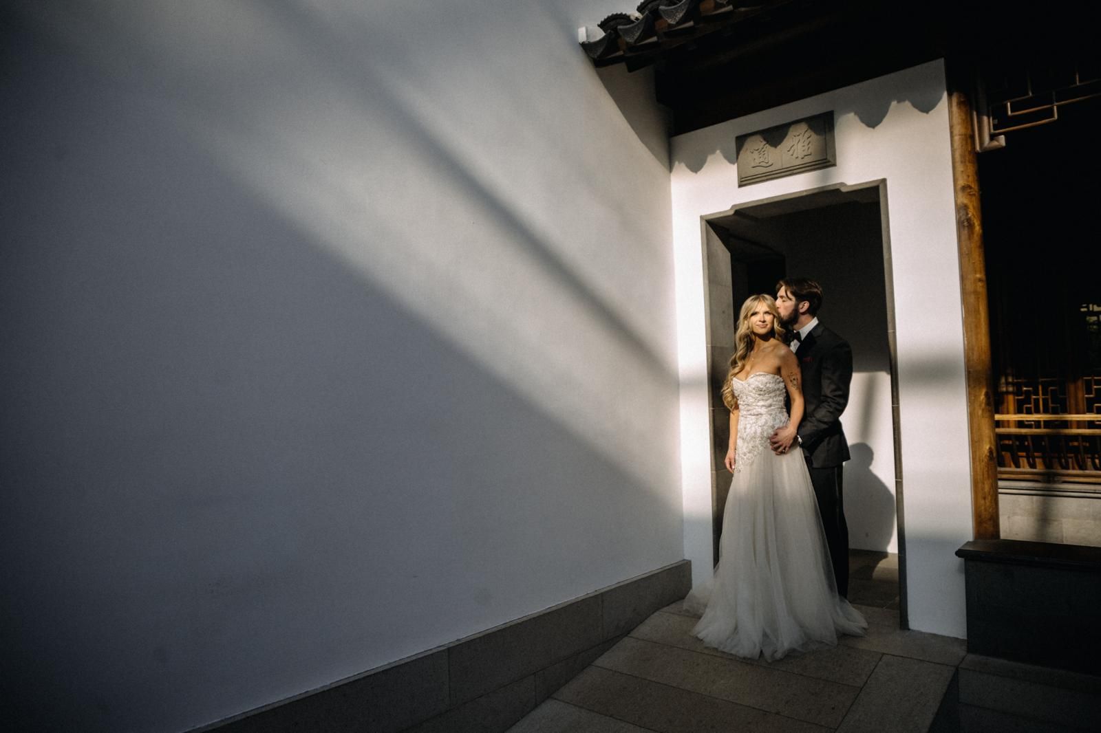 Bride and groom embracing in a doorway framed by dramatic light and shadow